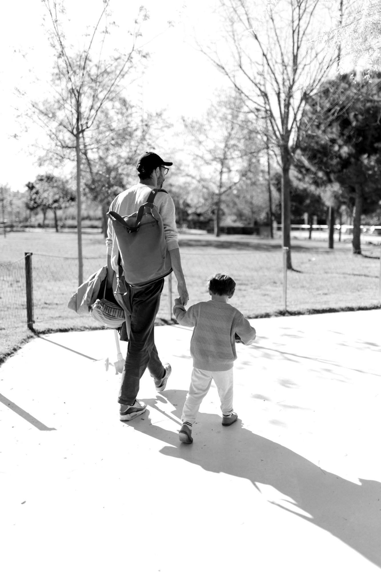 A father walks away holding hands with his young child in an open park.