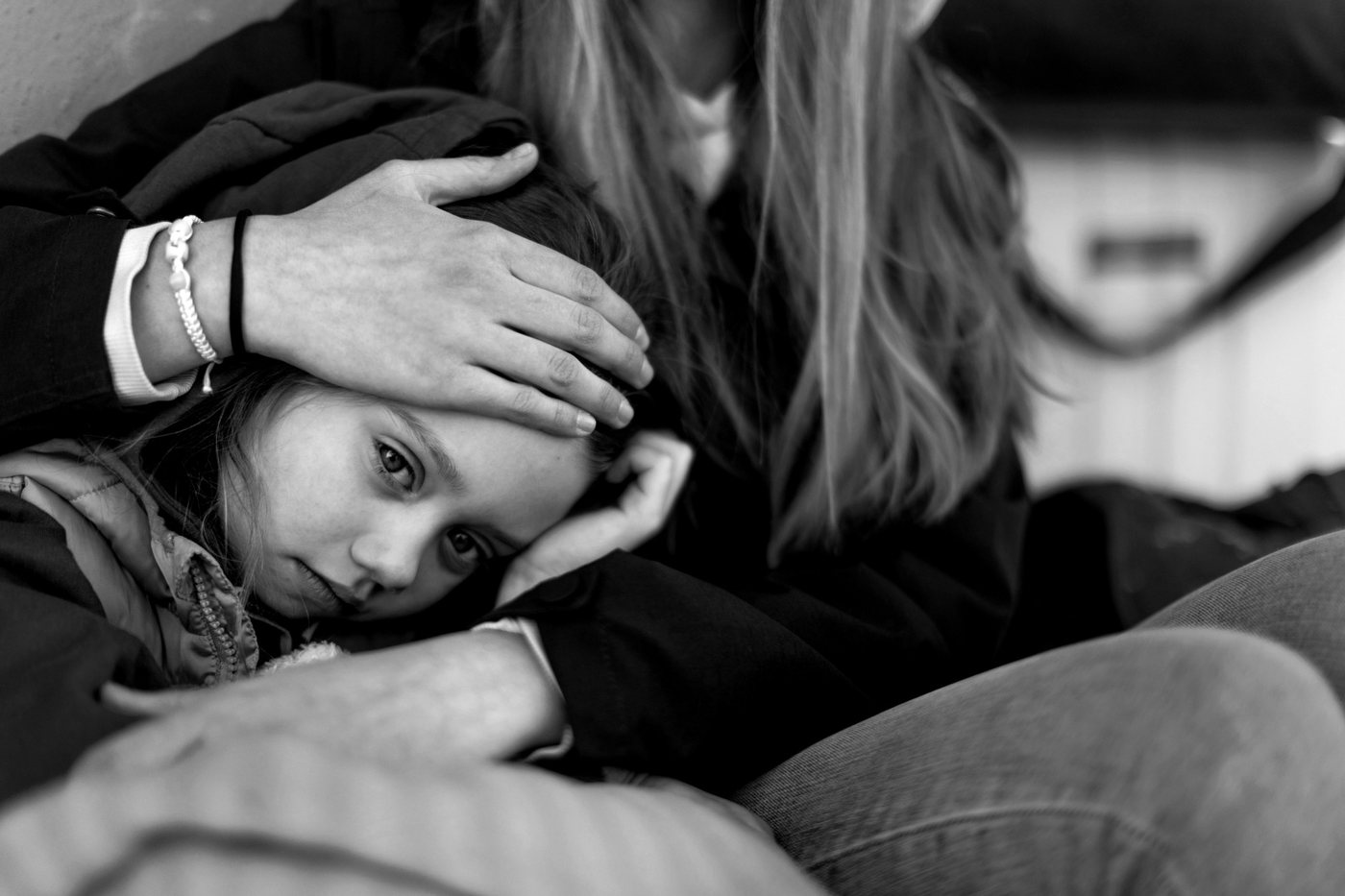 An adult protectively holds their hand over a child's head while the child looks toward the camera.