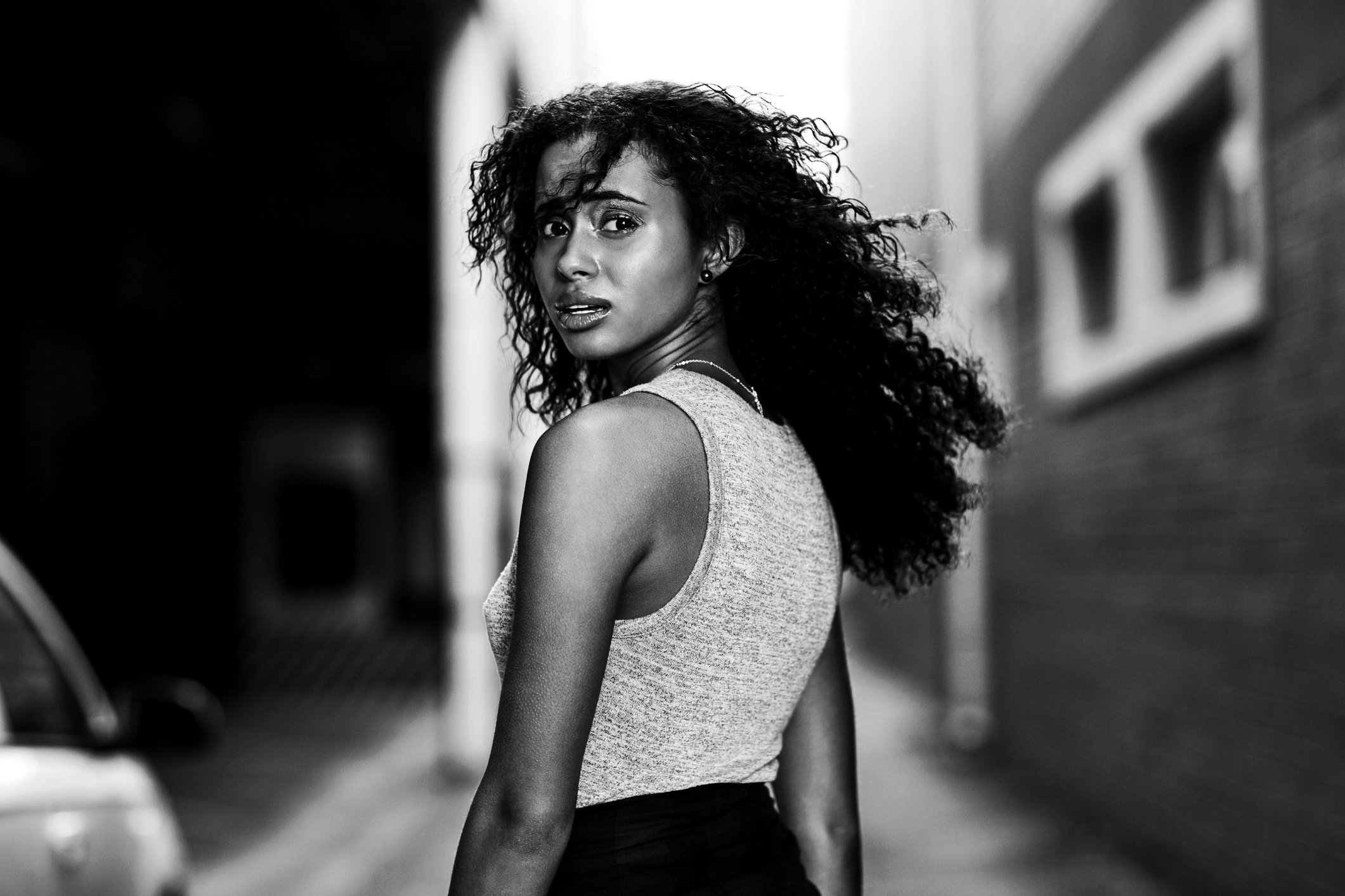 A woman with curly hair looks back over her shoulder while walking down a street.